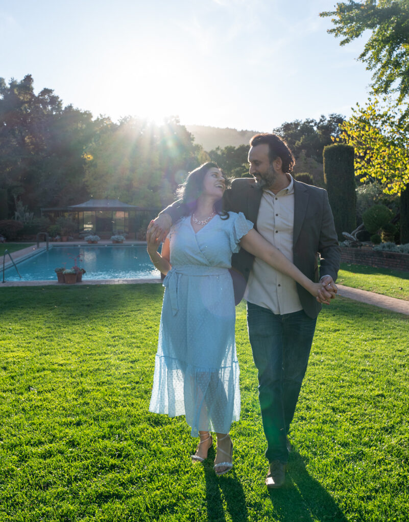 newly engaged Indian couple dancing in a field together while the bright sun shines behind them at Filoli Gardens in California